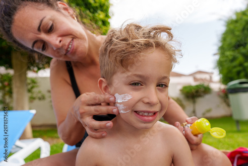 Mother applying sunscreen to young boy's face during summer vacation day, protecting skin from sun