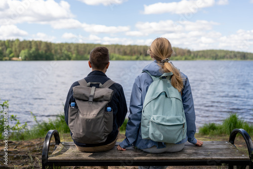 Back view of couple sitting on a bench by the lake and enjoying the peaceful view. Summer vacation, companionship and nature leisure concept