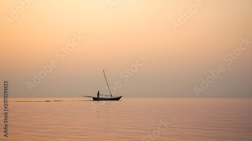 A lone sailboat glides across a calm sea during a serene sunset with warm orange hues.