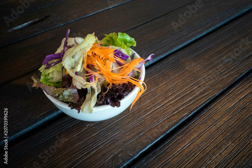 A vibrant colorful salad in a white bowl on an old dark wooden table