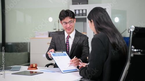 Professional Asian attorney explains legal contract terms to a businesswoman, leading to a successful deal and handshake in a modern law office workspace.