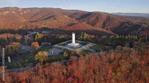 Aerial view of the SNP World War II memorial on Jankov Vrsok surrounded by autumn forest and rolling hills in warm evening light, Uhrovec, Slovakia