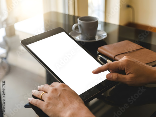 Close up of hand using digital tablet with blank white screen | Businessman operating touchpad tablet device at black office desk | Mockup screen on tablet computer with coffee cup and notebook 
