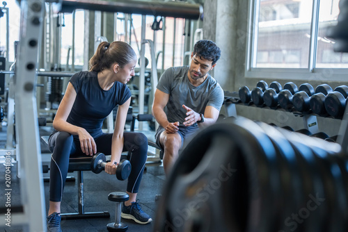 Personal trainer guiding a client in a gym environment using dumbbells and various fitness equipment for effective workouts