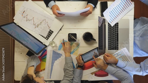 Young tired coworkers analyzing financial graphs at office. Group of exhausted colleagues work on business development sitting at table. Top view to male and female hands of managers. Slow motion