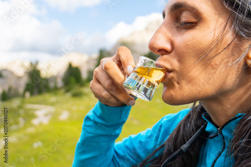 Φωτογραφία Close up woman traveler drinking local herbal spirit schnapps or grappa shot glass wooden terrace green mountain valley backdrop Dolomites Italy