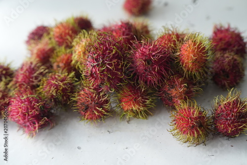 Fresh rambutans with vibrant red and pink skins are arranged together on a light background, showcasing their distinctive greenish-yellow soft spines. This image represents tropical freshness, natural