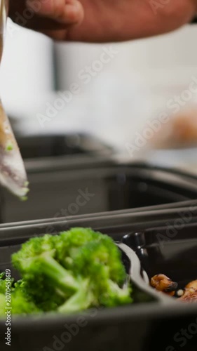 Vertical video: Entering hand scooping broccoli into black tray at counter, with spoon for prep