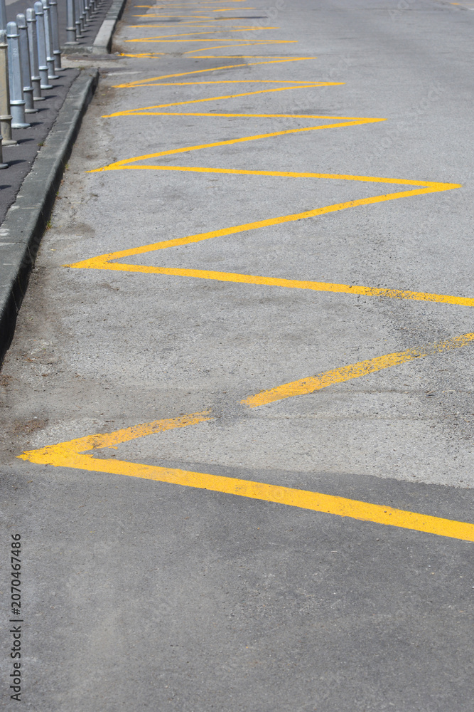 Obraz premium Yellow zig zag lines are painted on the grey asphalt road next to a pavement curb marking a no parking zone or bus stop