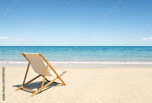 Wooden folding beach chair standing on a tropical white sand shoreline facing the calm turquoise ocean waves and clear blue horizon sky with vacation