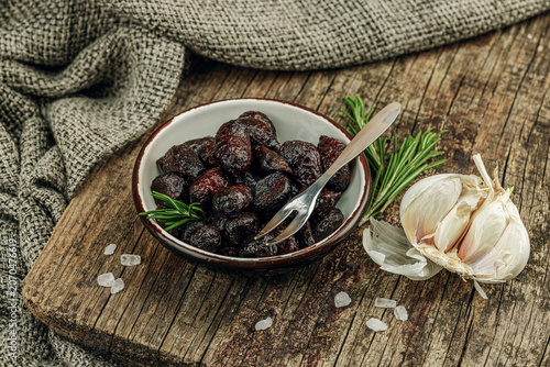 Black garlic cloves in oil with fresh rosemary branches and sea salt crystals in a ceramic bowl