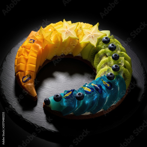 A colorful fruit tart with mango starfruit kiwi and blueberries on a plate