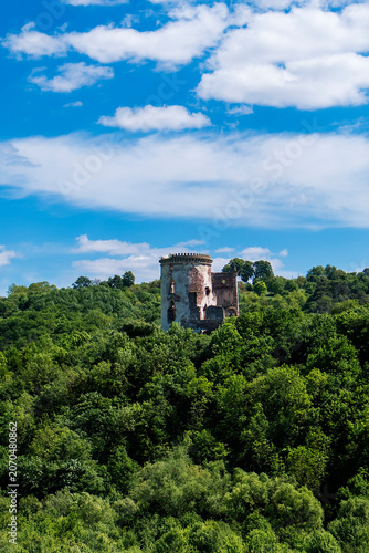 Historic ruined tower of Chervonograd Castle in Ukraine rising above lush green vegetation beneath a vibrant blue sky with scattered clouds.