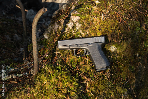 Bild auf Leinwand Modern black semi-automatic pistol lying on mossy concrete ruins with pine needles in a forest, tactical and military weapon concept