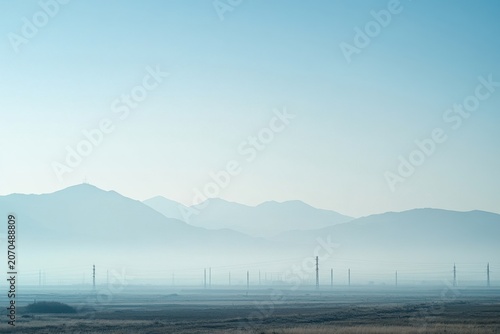 Smoggy horizon with barely visible mountain range and haze over rural plain, atmospheric sky and distant power line