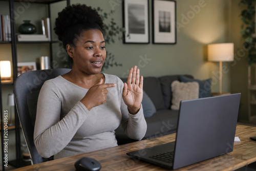 Woman communicates using sign language during a video call on her laptop computer at a desk in her home office.