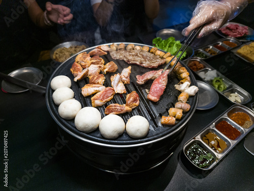 Grilling Assorted Meats and Dumplings on a Korean BBQ Grill with Side Dishes
