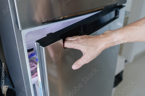 Close-up of adult male hand opening a modern stainless steel refrigerator door in a kitchen