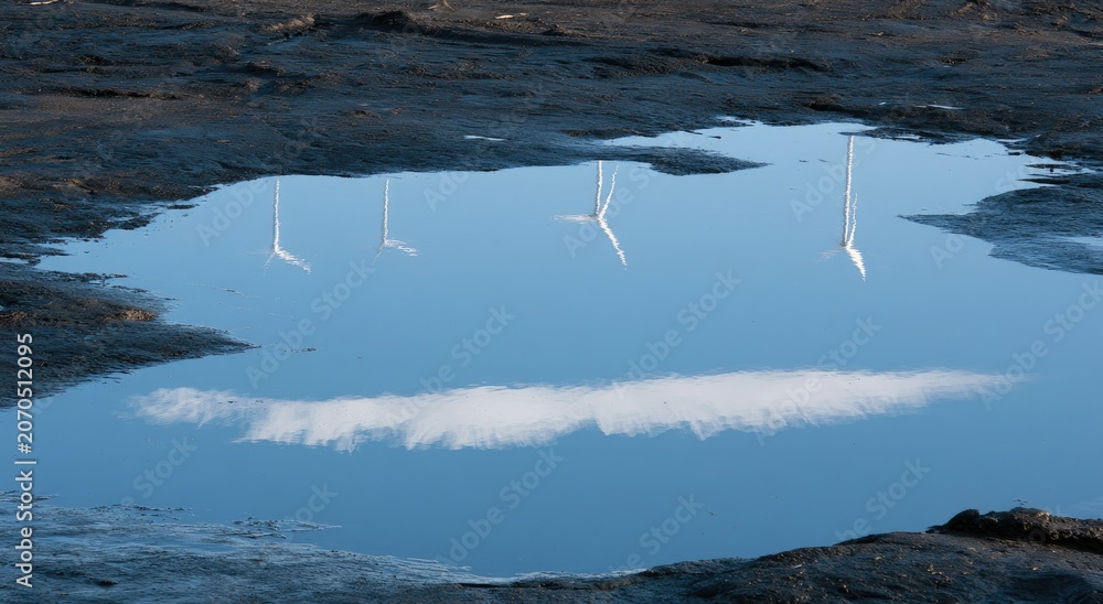 Fototapeta premium Reflection of wind turbines and clouds in a muddy puddle (1)