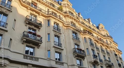 Cream colored ornate apartment building with balconies and shutters in sunlight cream facade