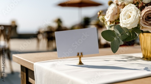 A white card sits on a table with a floral arrangement at an outdoor event