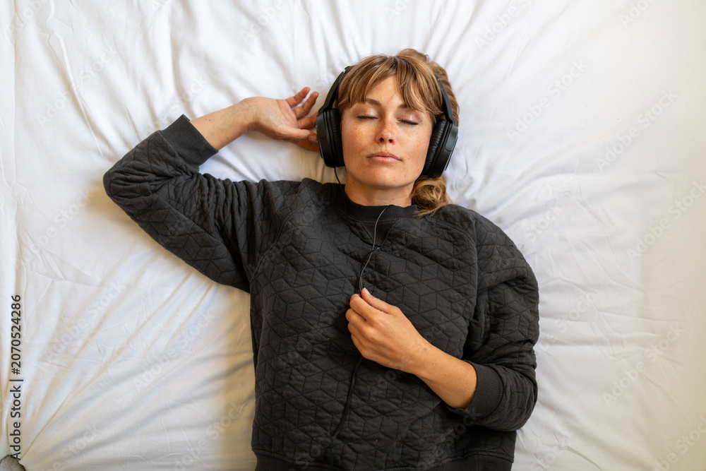Obraz premium Person relaxing on a bed, wearing headphones and a black sweater.