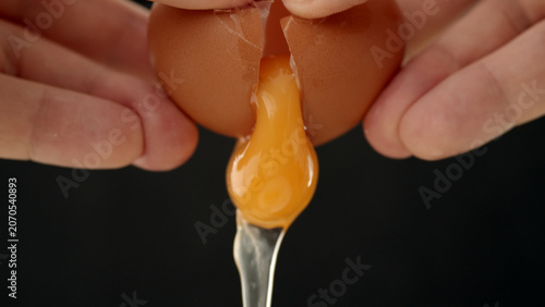 Canvas Print Close-up of hands cracking brown eggshell to release bright orange yolk into a m
