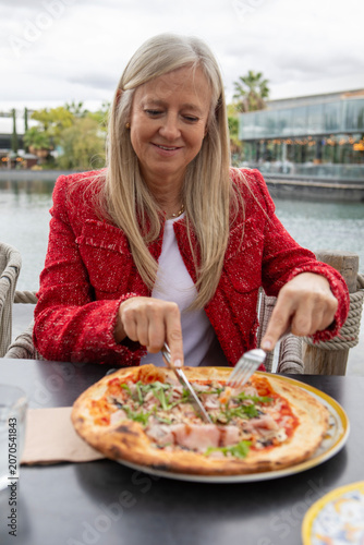 Fotografie Enjoying a delicious pizza by the serene lake while wearing a stylish red jacket