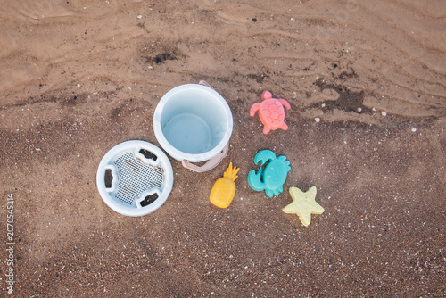 Colorful children's beach toys on wet sand by the seashore. Bucket, sieve and sea animal molds on the beach, summer vacation and family holiday concept.
