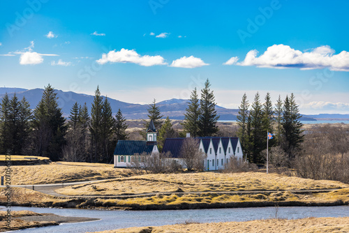 Small Icelandic church near river with mountain landscape and blue sky background