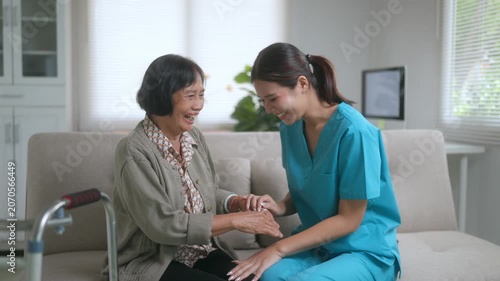 Professional caregiver providing compassionate support and encouragement to an elderly patient, holding her hands and sharing a laugh while sitting on the living room sofa during a home visit