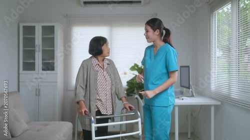 Friendly asian nurse helping a senior woman use a walker for physical therapy and mobility support inside a modern nursing home, providing comfort, assistance, and encouragement during her recovery