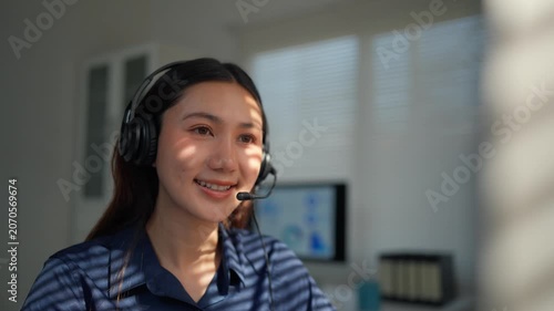 Friendly asian female customer service representative wearing a headset with a microphone, talking to a client in a sunlit office, providing helpful and efficient telemarketing assistance