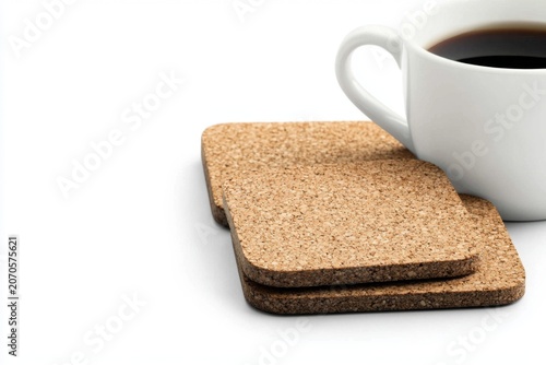White ceramic coffee cup filled with fresh black coffee placed on cork coasters on a clean white background, close-up, minimalistic, morning breakfast scene
