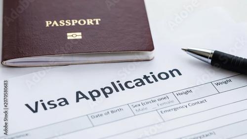 A close-up view of a travel visa application form lying on a desk with a passport and a black ballpoint pen ready for completion of identity information