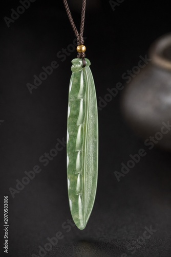 A slender green jade pendant shaped like a silique on a dark background.
