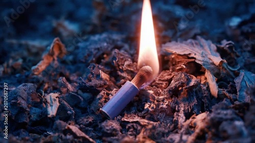 Lit match ignites in a bed of ashen debris. Flame glows, illuminating surroundings