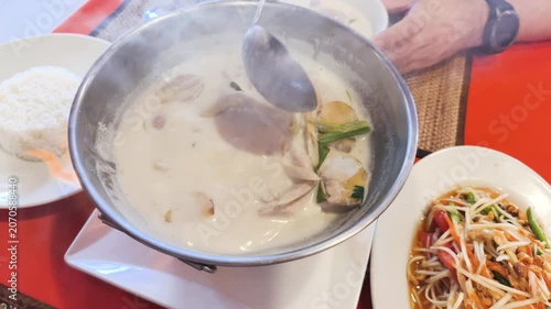 Traditional Asian hot pot dinner features rich soup boiling over open fire. This festive Asian hot pot dinner includes healthy side dishes like white rice and fresh salad on restaurant table.