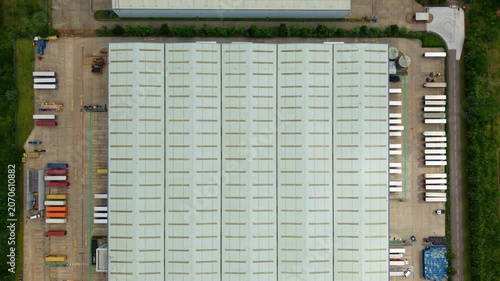 Top down aerial view of a large commercial distribution centre warehouse with rows of HGV lorries parked in loading bays.
