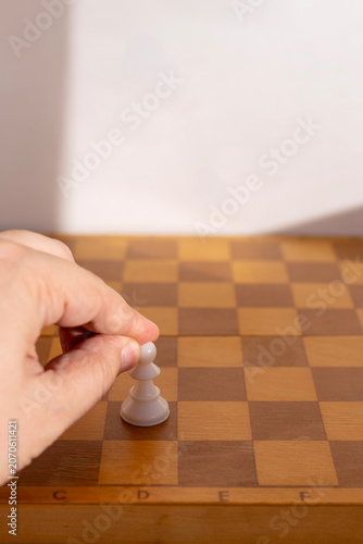 Foto A person's hand placing a single white chess pawn on an empty wooden chessboard