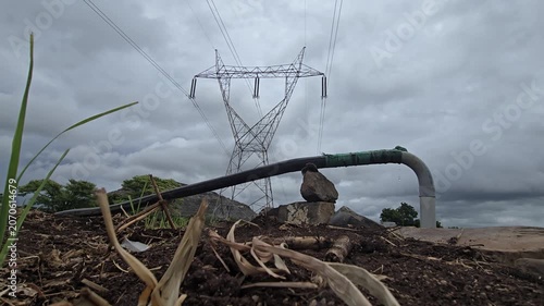 A dramatic overcast timelapse: Electricity pylon clouds signal a rain delay. Agricultural irrigation pipeline boosts sugarcane plantation soil health facing weather uncertainty & energy power crisis.