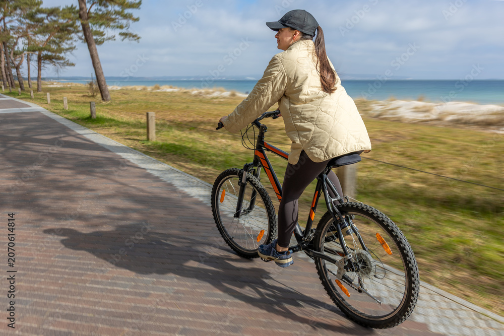 Fototapeta premium Woman cycling beside the sea. Active outdoor recreation on coastal path.