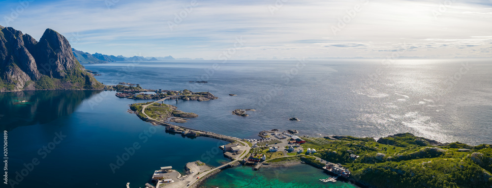 Obraz premium Aerial view of Lofoten near Reine and Reinebringen ridge, steep peaks left, small islands and bridges, turquoise coves, fishing village, causeway, calm water, Arctic light.