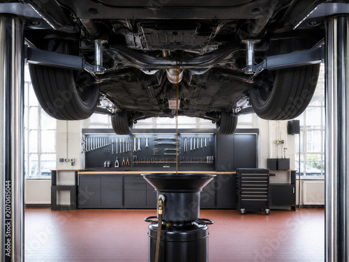 Vehicle underside on a lift during an oil change, with motor oil draining into a pan in a bright auto service workshop.