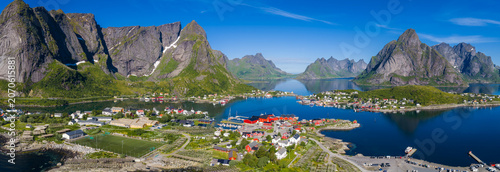 Foto Aerial daylight view of Reine, Lofoten Islands, Norway, with crimson rorbuer by a fjord, Reinebringen peaks, bridges over calm water, harbors, and snow patches