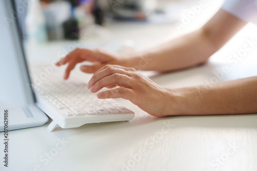 Female worker typing on modern white keyboard in clinic