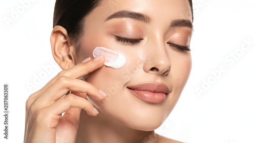 Elegant woman applying luxury skincare cream on face with soft studio lighting on clean white background