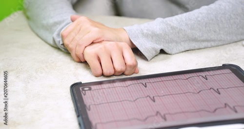 Close-up of a person gently massaging their own wrist beside a tablet displaying an ECG waveform. Self care, wrist pain relief, hand fatigue recovery, home healthcare, and wellness concept.