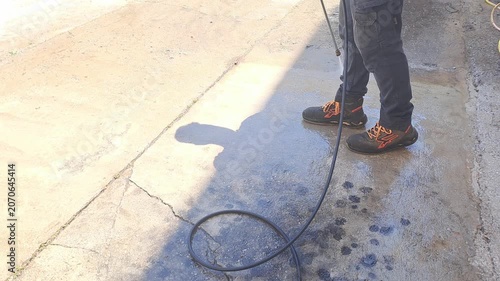 Worker is cleaning a dirty concrete surface outdoors using a high-pressure water washer