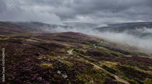 Winding mountain road through misty highland landscape under dramatic cloudy sky.
